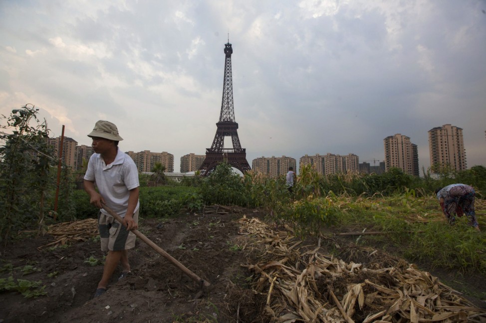 Farmer tills field under a replica of Eiffel Tower at the Tianducheng development in Hangzhou