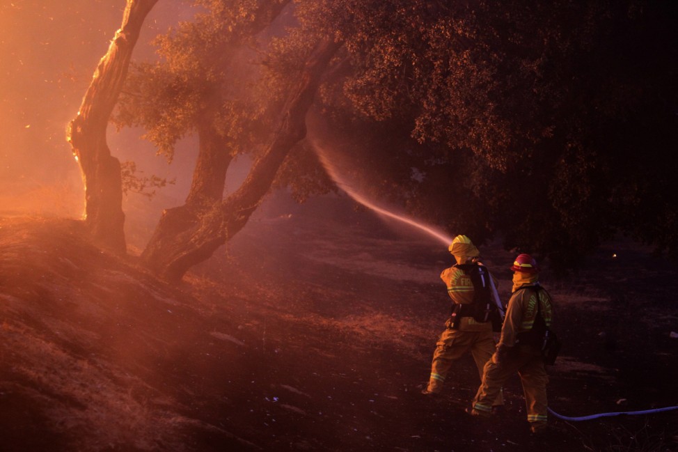 Firefighters spray water near a burning house in the Twin Pines Road area at the Silver Fire near Banning, California.