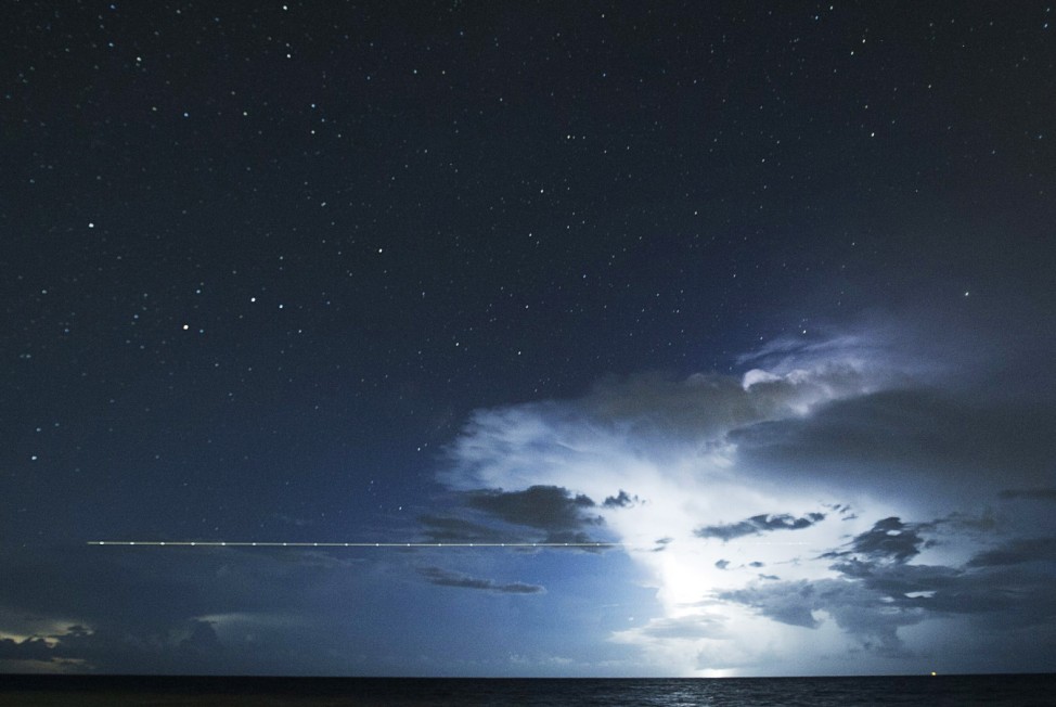 A long exposure shot shows a plane flying over the sea during a lightning storm on the last day of the annual Perseid meteor shower, near Cancun