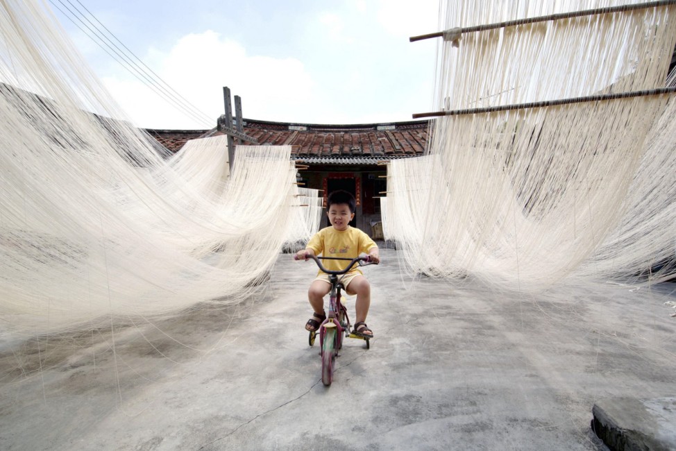 A boy rides a bicycle in between home-made rice noodles in Changting county