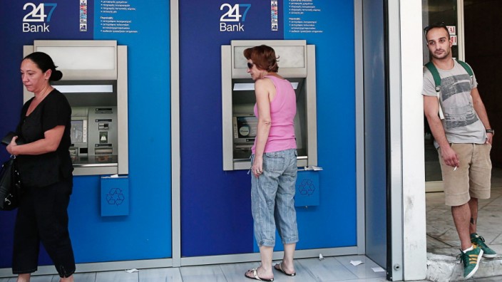 People make transactions at ATM machines outside a bank branch in Athens