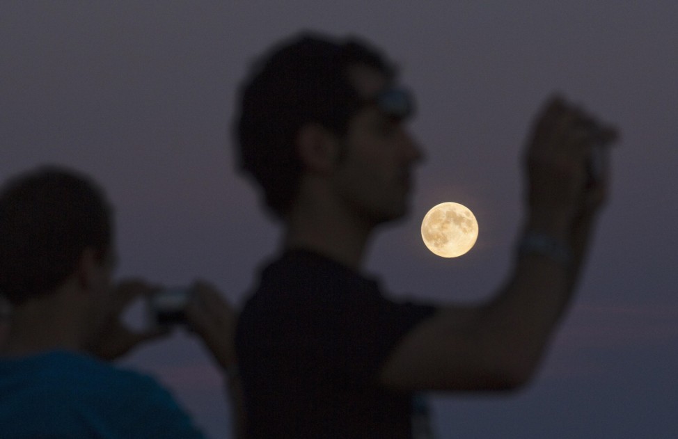People watch the moon rise just after sunset from a viewpoint on Cypress Mountain in West Vancouver
