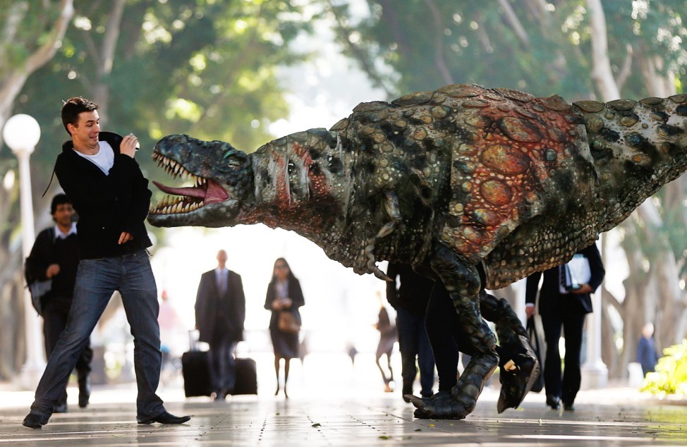 A man reacts as a performer dressed in a Tyrannosaurus rex dinosaur costume walks next to him during a publicity event in central Sydney