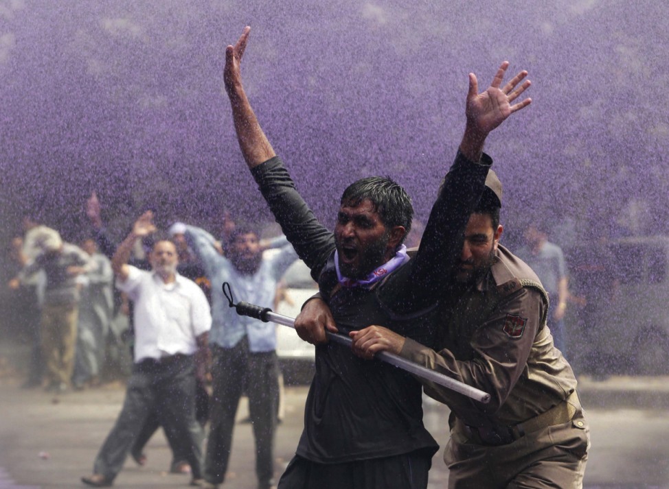 An Indian policeman detains a government employee during a demonstration in Srinagar