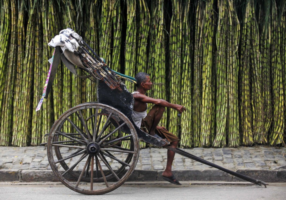 A hand-rickshaw puller waits for customers at a roadside wholesale sugarcane market in Kolkata