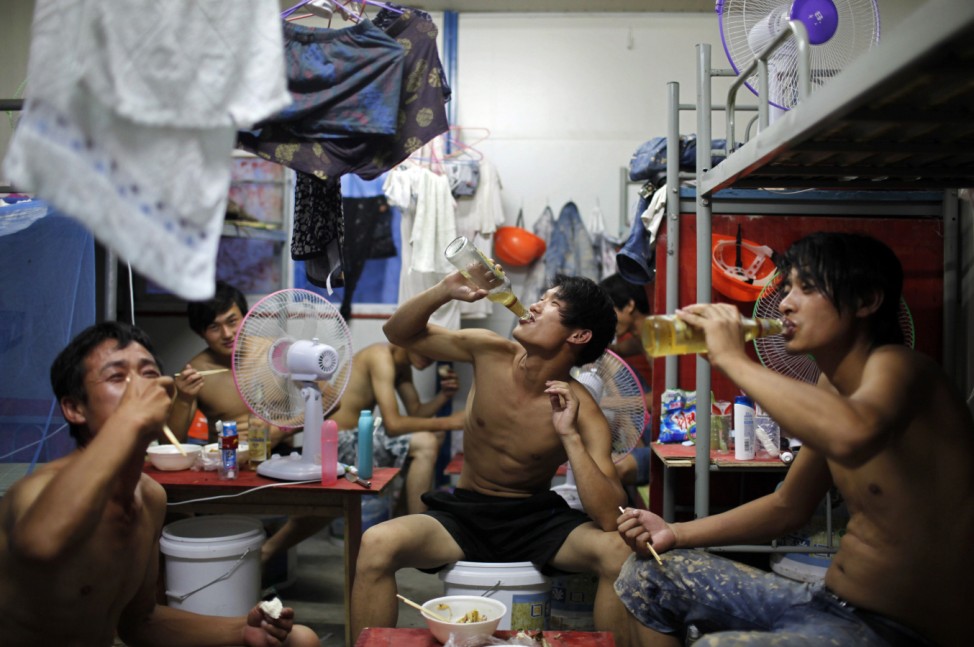 Migrant construction workers drink beer during a meal inside their dormitory after a shift at a residential construction site in Shanghai