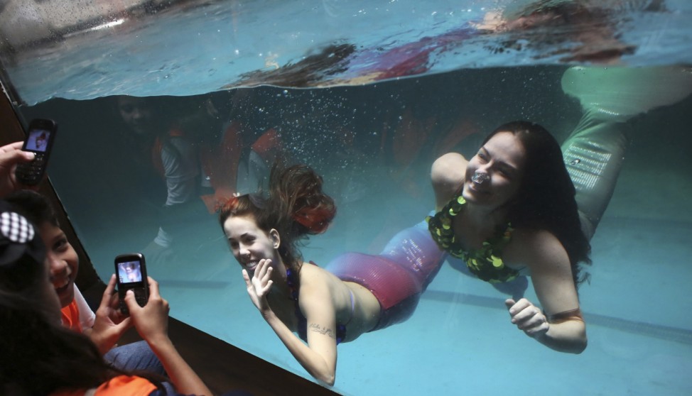 Women dressed as sirens perform from inside tank as school children use mobile phones to photo of them at the Sao Paulo Aquarium
