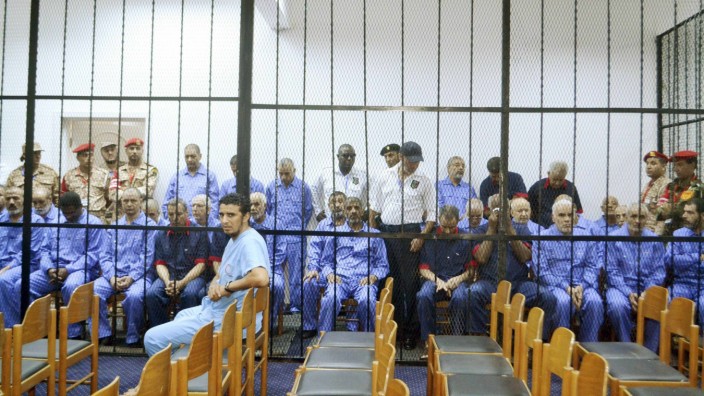 Officials of the former Muammar Gaddafi government sit behind bars during a hearing at a courtroom in Tripoli