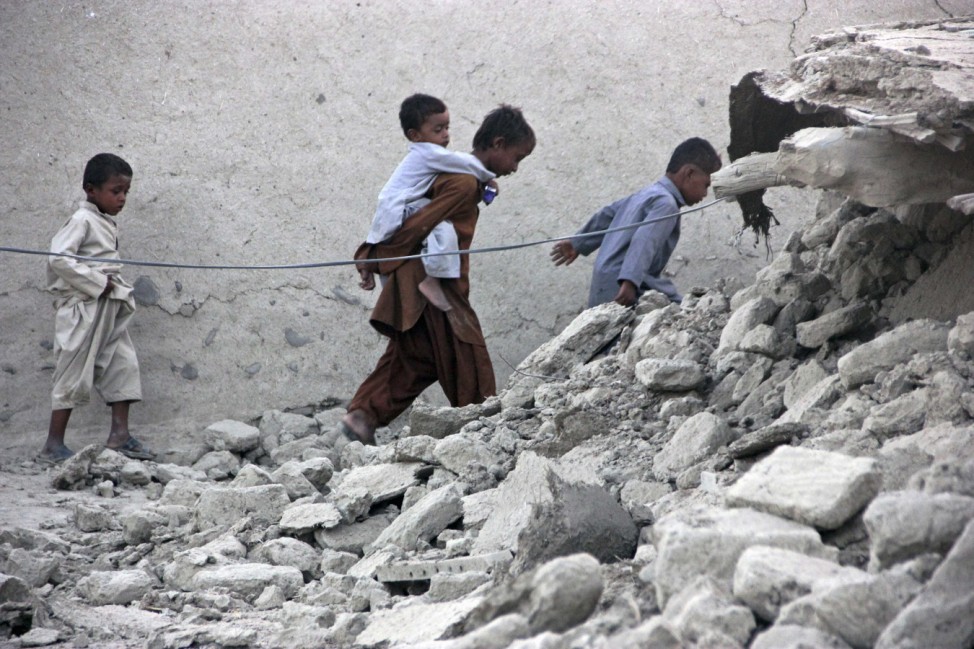 Survivors of an earthquake walk on rubble of a mud house after it collapsed following the quake in the town of Awaran