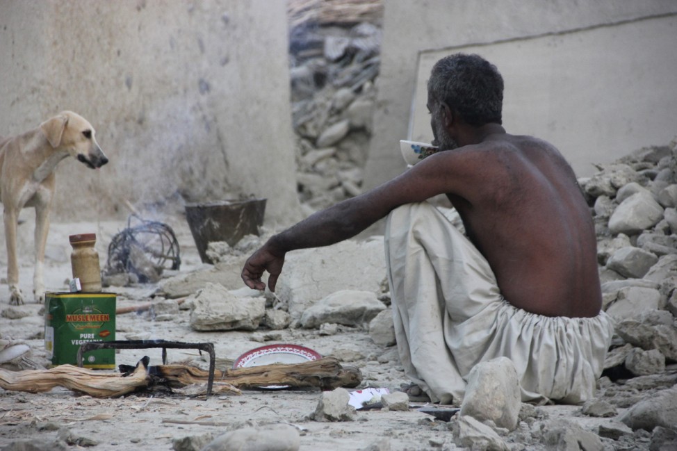 A survivor of an earthquake sits as he takes tea on rubble of a mud house after it collapsed following the quake in the town of Awaran