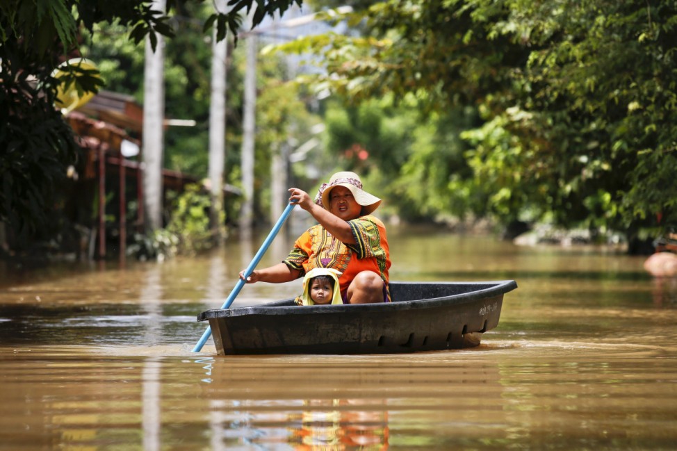 A woman and her child travel along a flooded street by boat at Kabin Buri district in Prachin Buri