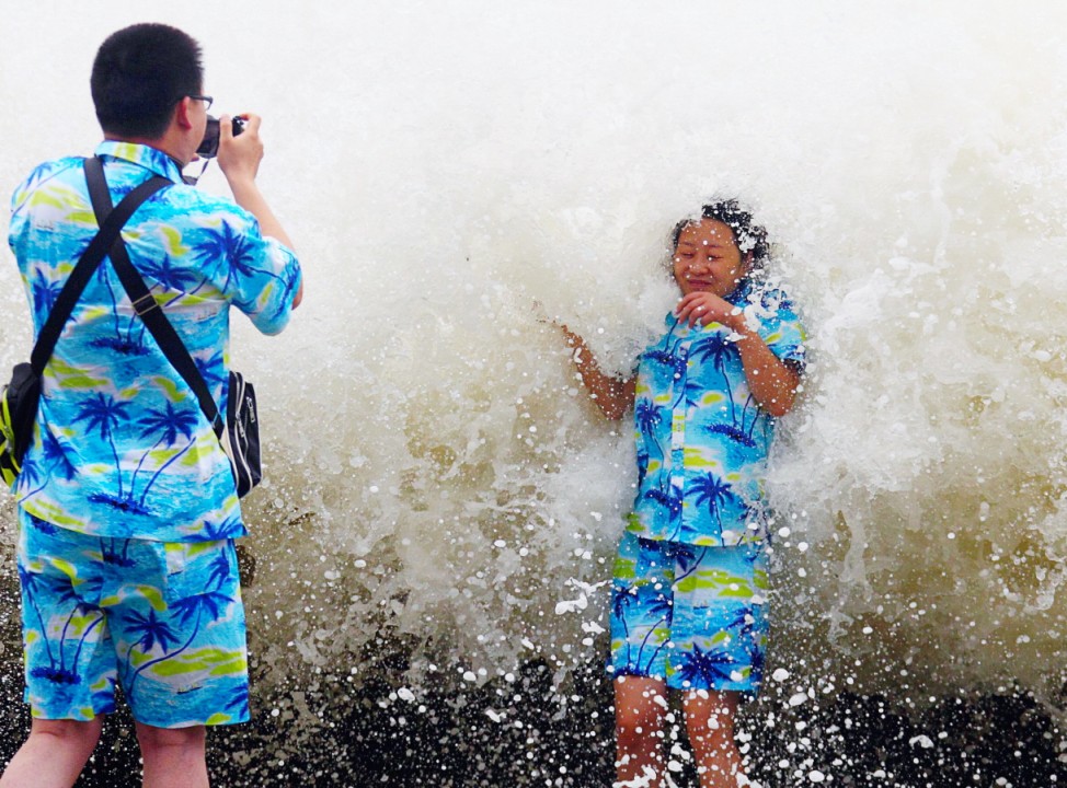 Tourists take pictures as a storm surge hits the coastline under the influence of Typoon Wutip in Sanya
