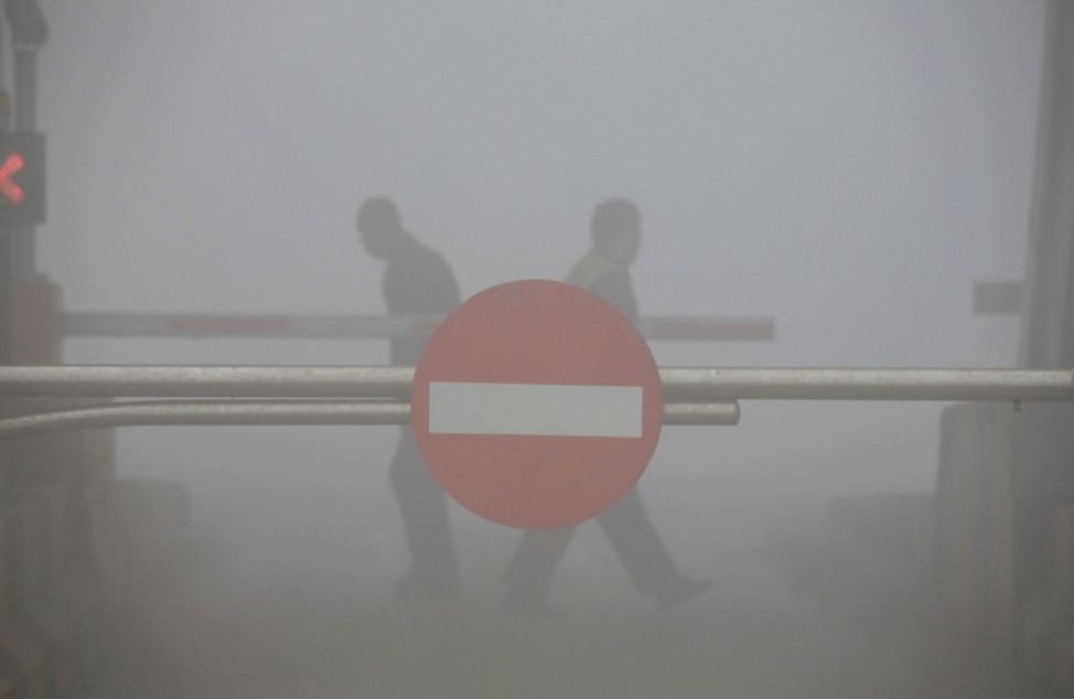 People walk behind a road sign at a closed toll gate on a highway in Jilin city