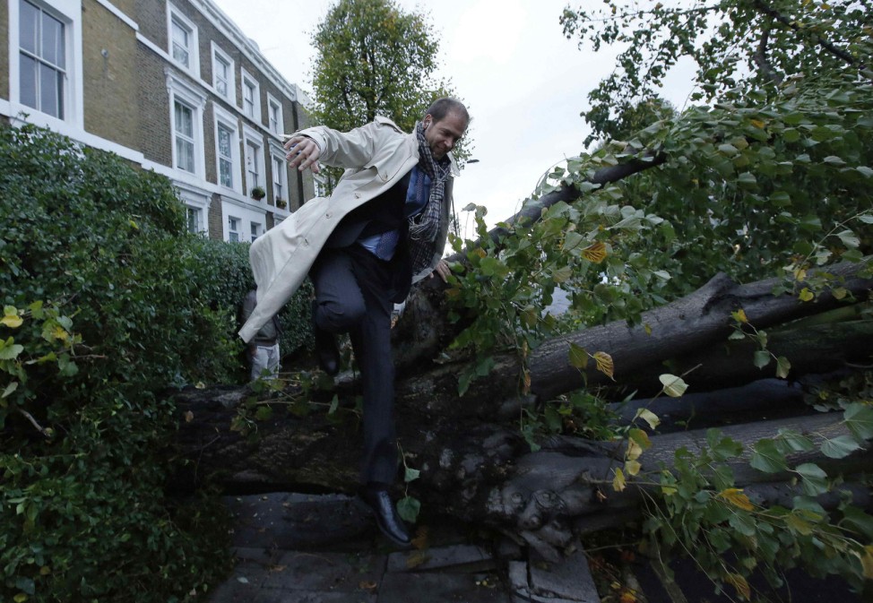 A man jumps over a fallen tree on his way to work in Islington, north London