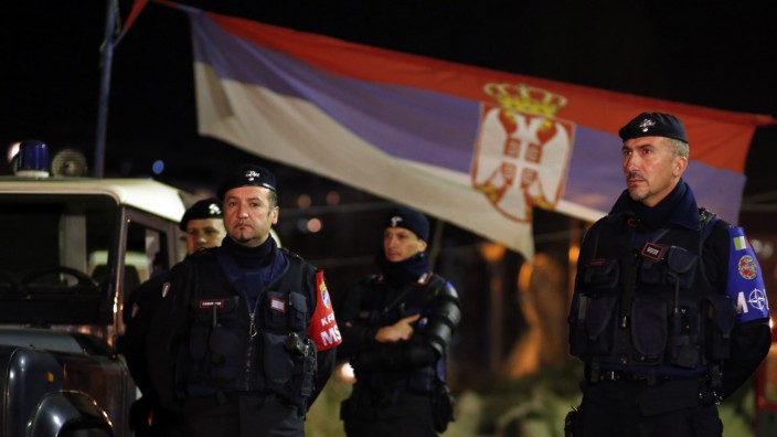 Italian Carabinieri, who are members of NATO's KFOR, stand in front of a Serbian national flag as they secure the main bridge in the northern part of Mitrovica