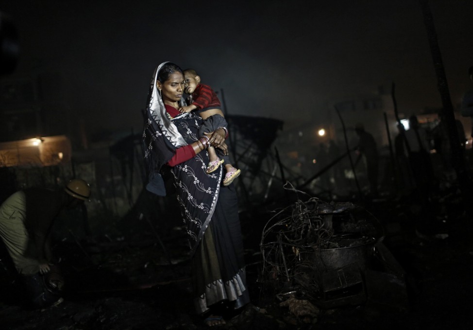 A slum dweller carries her child while standing next to her burnt belongings after a fire that broke out at a slum area in New Delhi