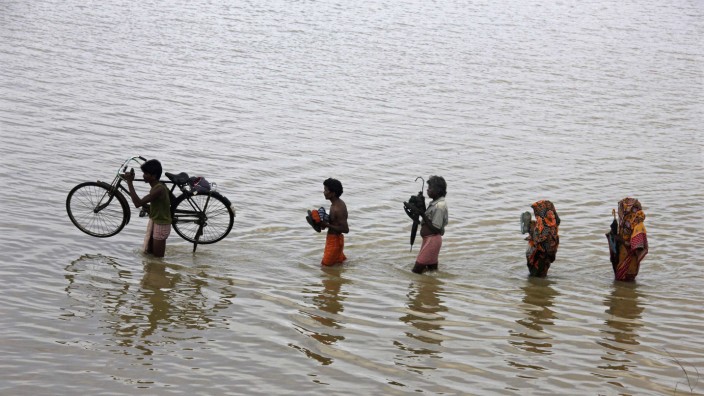 People from a nearby village carry their belongings through floodwaters at Ganjam district in Odisha