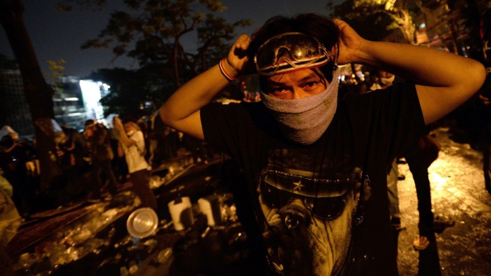 Anti-government protesters take cover from tear gas as they attack Government House during demonstrations in Bangkok