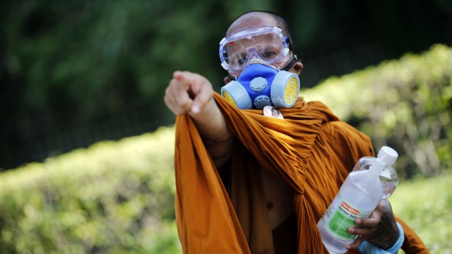 A Buddhist monk wearing a gas mask points towards police positions as they clash with anti-government protesters near the Government House in Bangkok