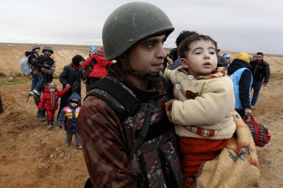 Jordanian soldier carries a Syrian refugee child as they walk with Syrian refugees near Ruwaished