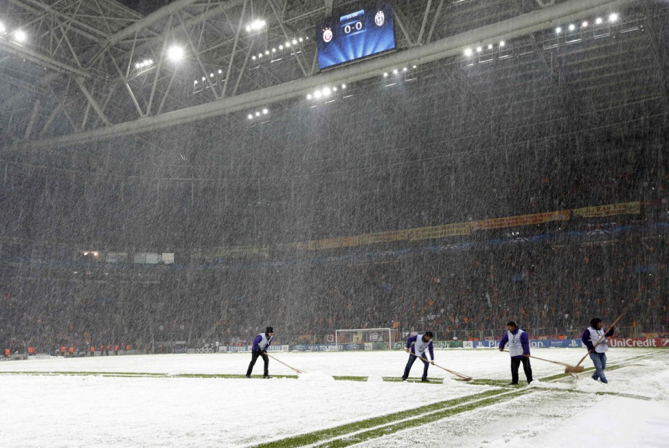 Workers rush to clean the snow from the pitch after the Champions League soccer match between Galatasaray and Juventus was paused for 20 minutes due heavy snowfall in Istanbul