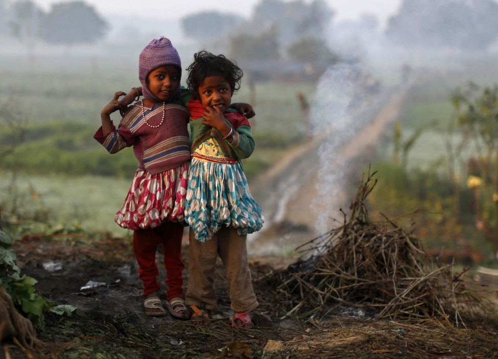Girls stand near smoke from twigs which were set on fire by their parents to warm themselves at a vegetable field in New Delhi