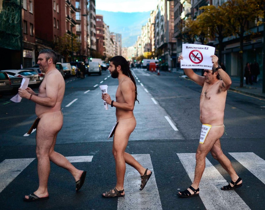 Naked protesters walk through Bilbao carrying signs reading 'No To Social Services Cuts'