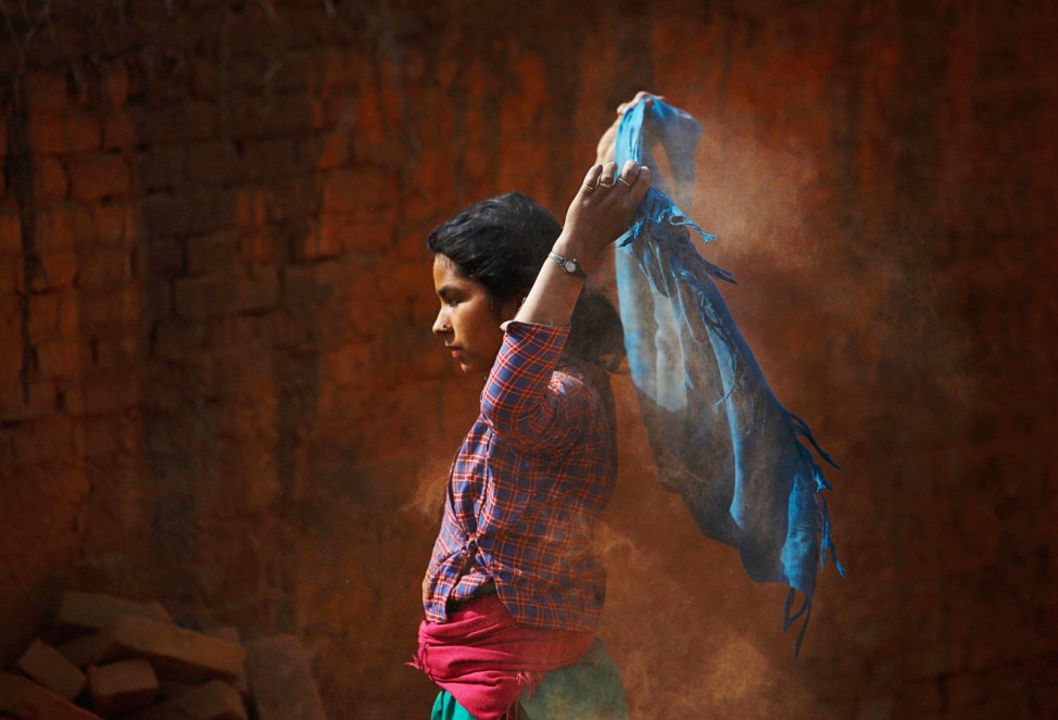 A girl removes dust from scarf as she works to earn money by carrying bricks at brick factory in Lalitpur