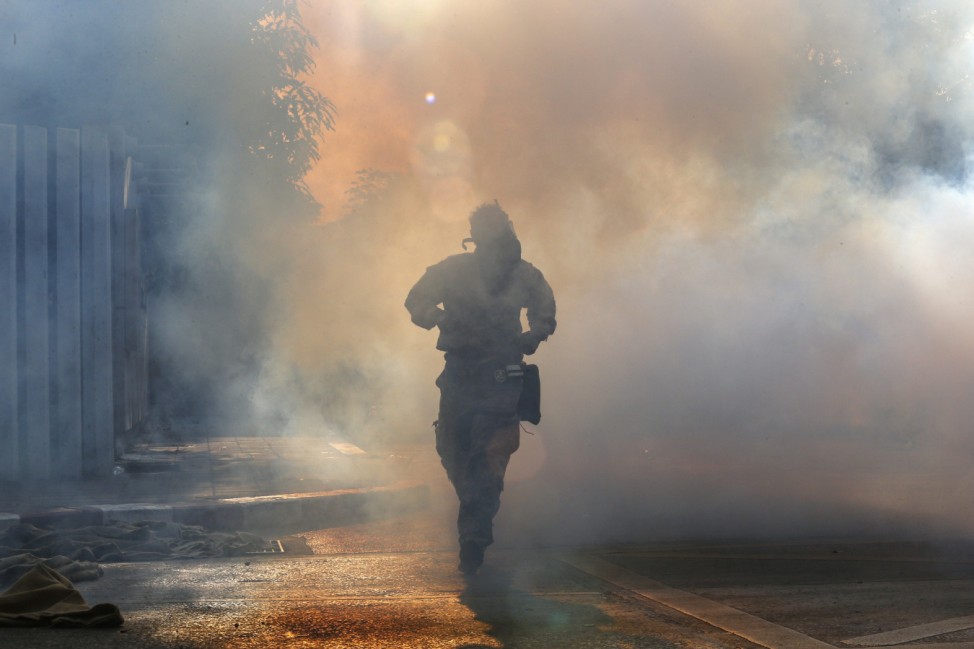 An anti-government protester runs away from teargas fired by riot police during clashes with policemen at the Thai-Japan youth stadium in central Bangkok