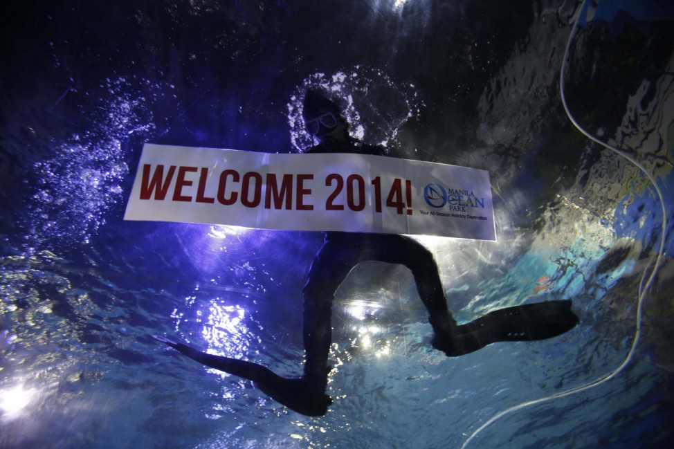 A professional diver holds a 'Welcome 2014' banner inside a large aquarium at a ocean park in Manila