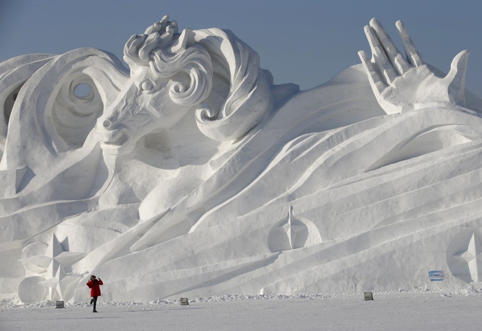 A woman poses for a picture in front of a large snow sculpture ahead of the Harbin Ice and Snow Sculpture Festival in the northern city of Harbin