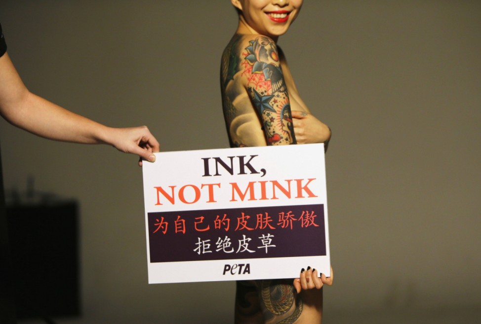 A staff member adjusts sign as naked Chinese tattoo artist and model Wang shows off tattooed back during advertising shoot for PETA Asia, in Beijing