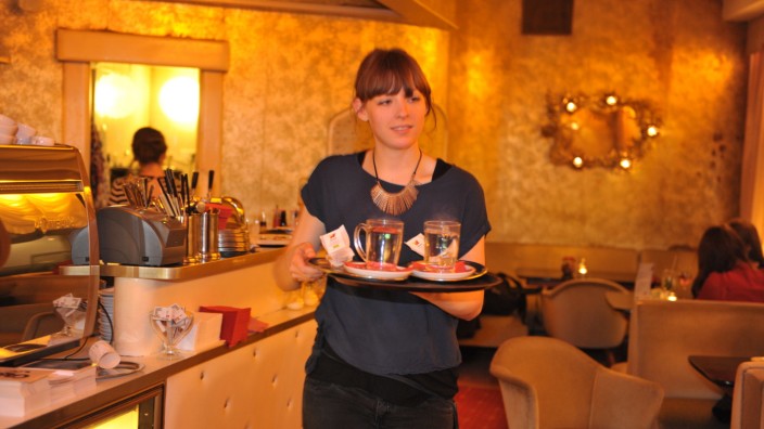 Szene München: Eine Kellnerin bringt den Tee. Ob sie die Leute beim Servieren berührt hat, wissen wir nicht.