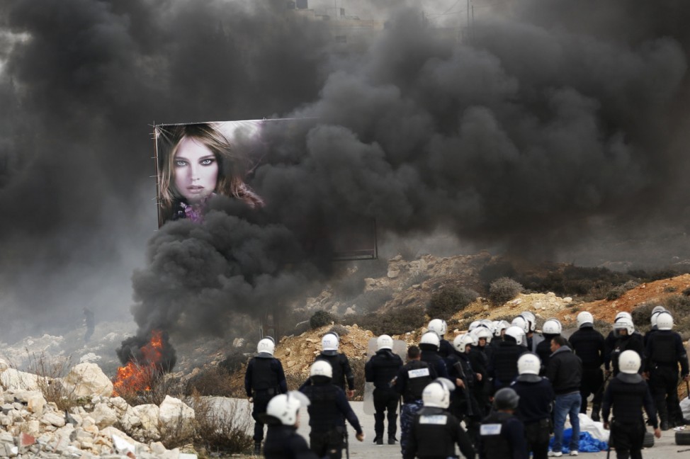 Palestinian policemen stand near burning tyres set ablaze by demonstrators outside Jalazoun refugee camp near Ramallah