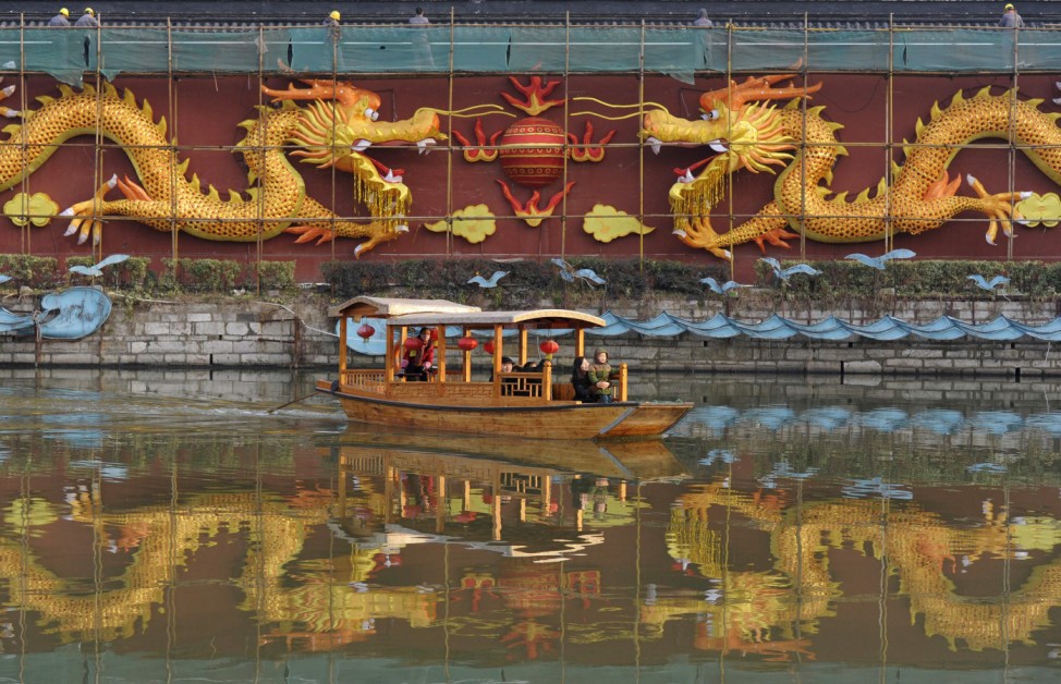 Workers install illumination on a wall decorated with two dragons as tourists row past in a boat on Qinhuai River in Nanjing