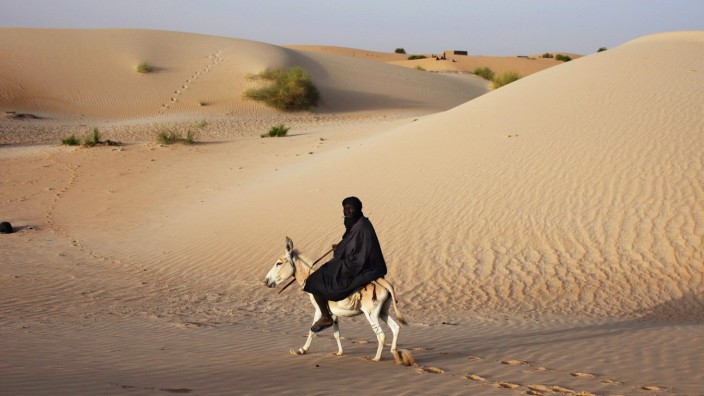 A herder rides a donkey next to sand dunes on the outskirts of Timbuktu