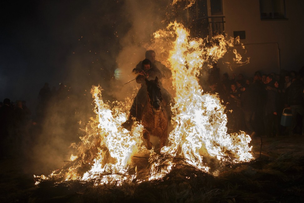 A man rides a horse with a child through the flames during the 'Luminarias' annual religious celebration in San Bartolome de los Pinares