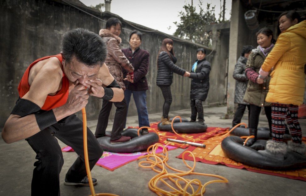 Nie Yongbing blows tires with air out of his nose as people stand on them in Chengdu