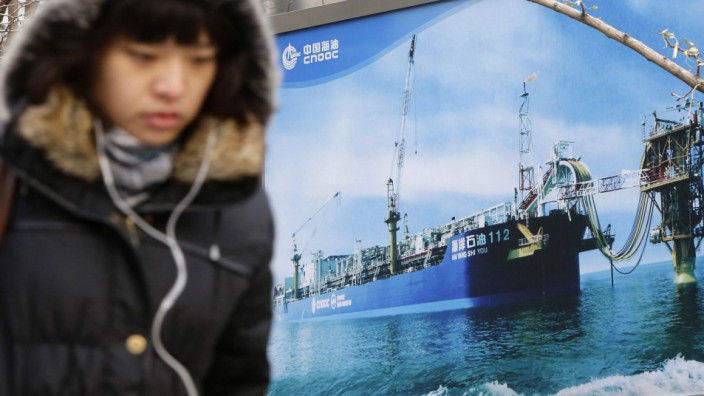 A woman walks past a poster showing an offshore work platform from CNOOC in Beijing