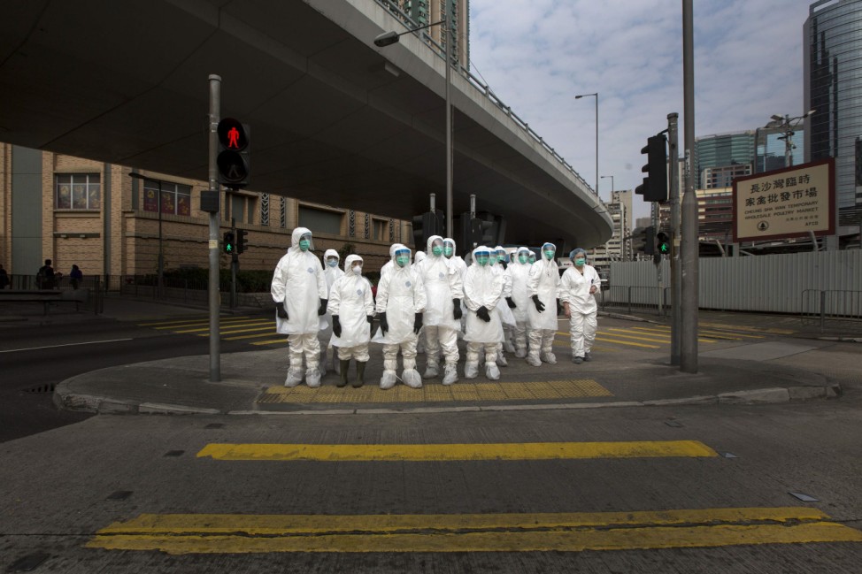 Health officers in full protective gear wait to cross a road near a wholesale poultry market in Hong Kong