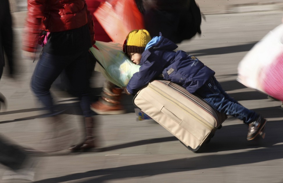 A person drags a suitcase as a boy clings to it on a square in front of a railway station ahead of the Chinese Lunar New Year in Qingdao