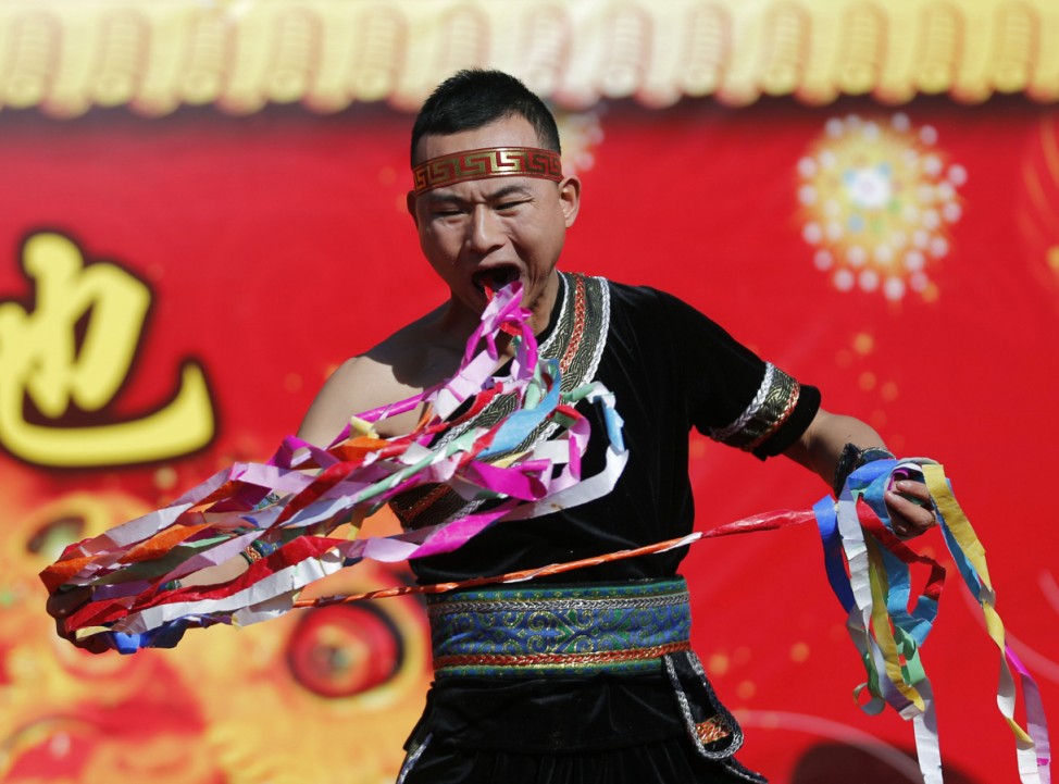 A man pulls ribbons from his mouth as he performs a feat of his strength during the opening of the temple fair in Beijing