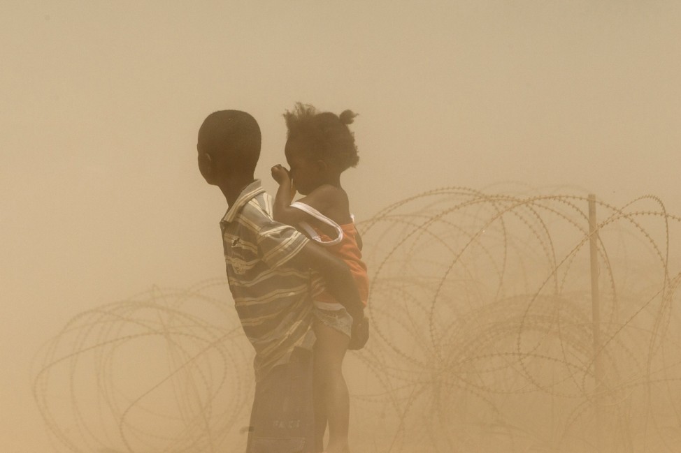 Children are engulfed in dust as a convoy arrives at a IDP camp at the airport in Bangui