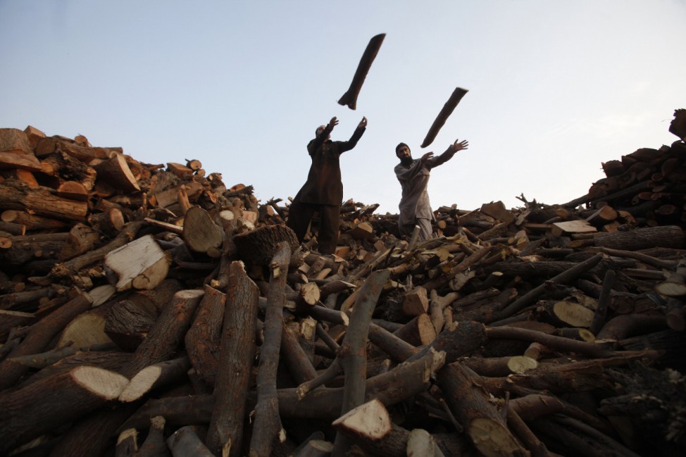 Men throw wood from a pile of logs into a supply truck at a timber warehouse in Lahore