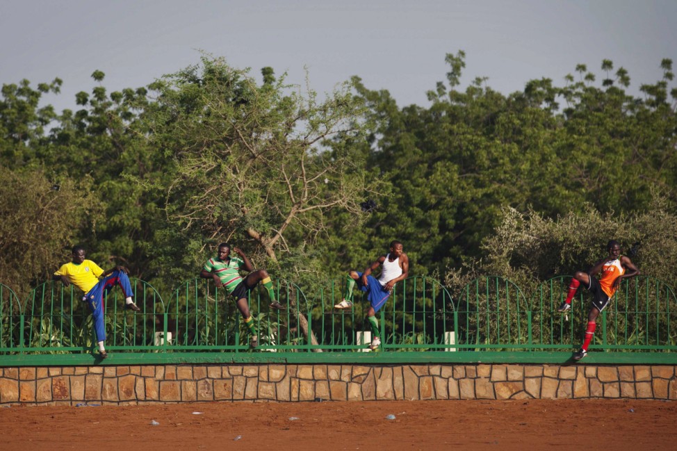 Soccer players, perched on a fence, watch a pick-up game in Niamey