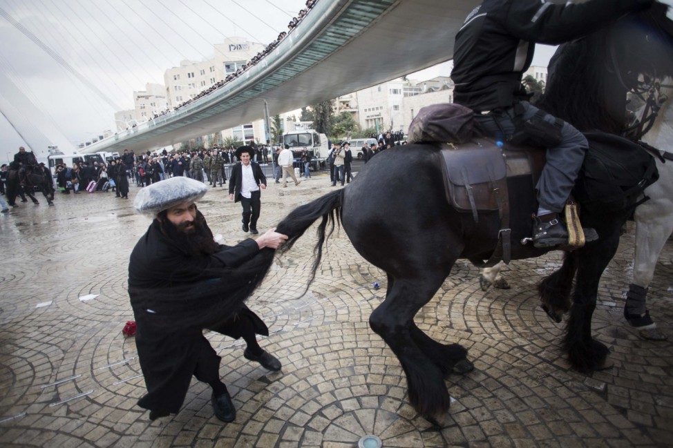 An ultra-Orthodox Jewish protester pulls the tail of a horse used by policemen to disperse protesters during a demonstration in Jerusalem