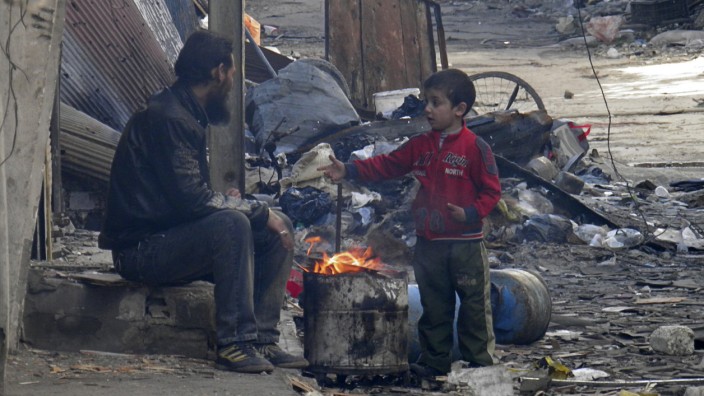 A child gestures as he stands next to a fire in the besieged area of Homs