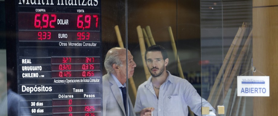 Two men stand next to a exchange billboard showing the official U.S dollar rate to Argentine pesos in Buenos Aires