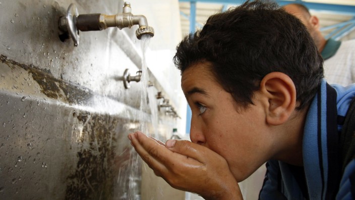 A Palestinian youth drinks water from a public tap in Khan Younis in Gaza