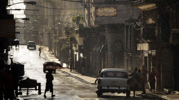 People board a U.S.-made car, used as a private collective taxi, as it rains in Havana